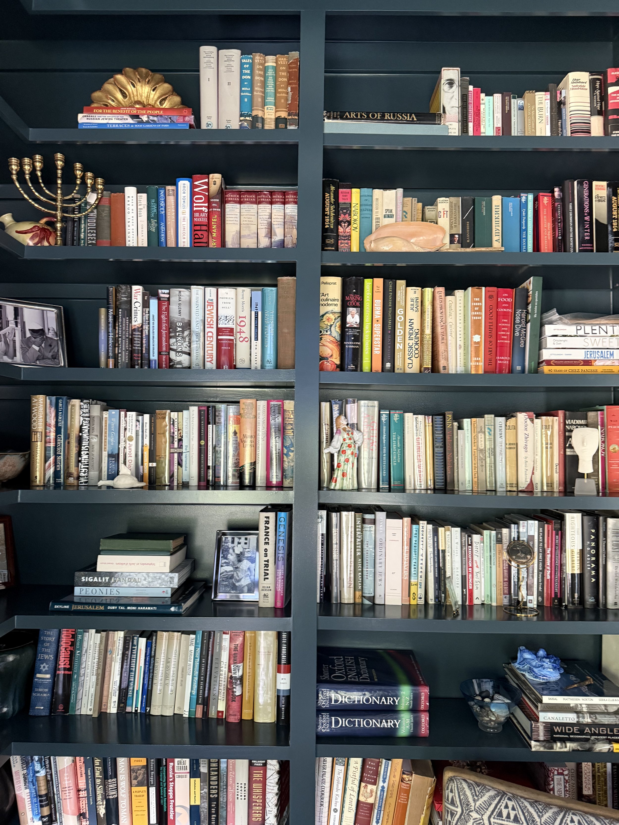 A dark blue bookshelf filled with books, decorative items, photographs, a menorah, and small sculptures.